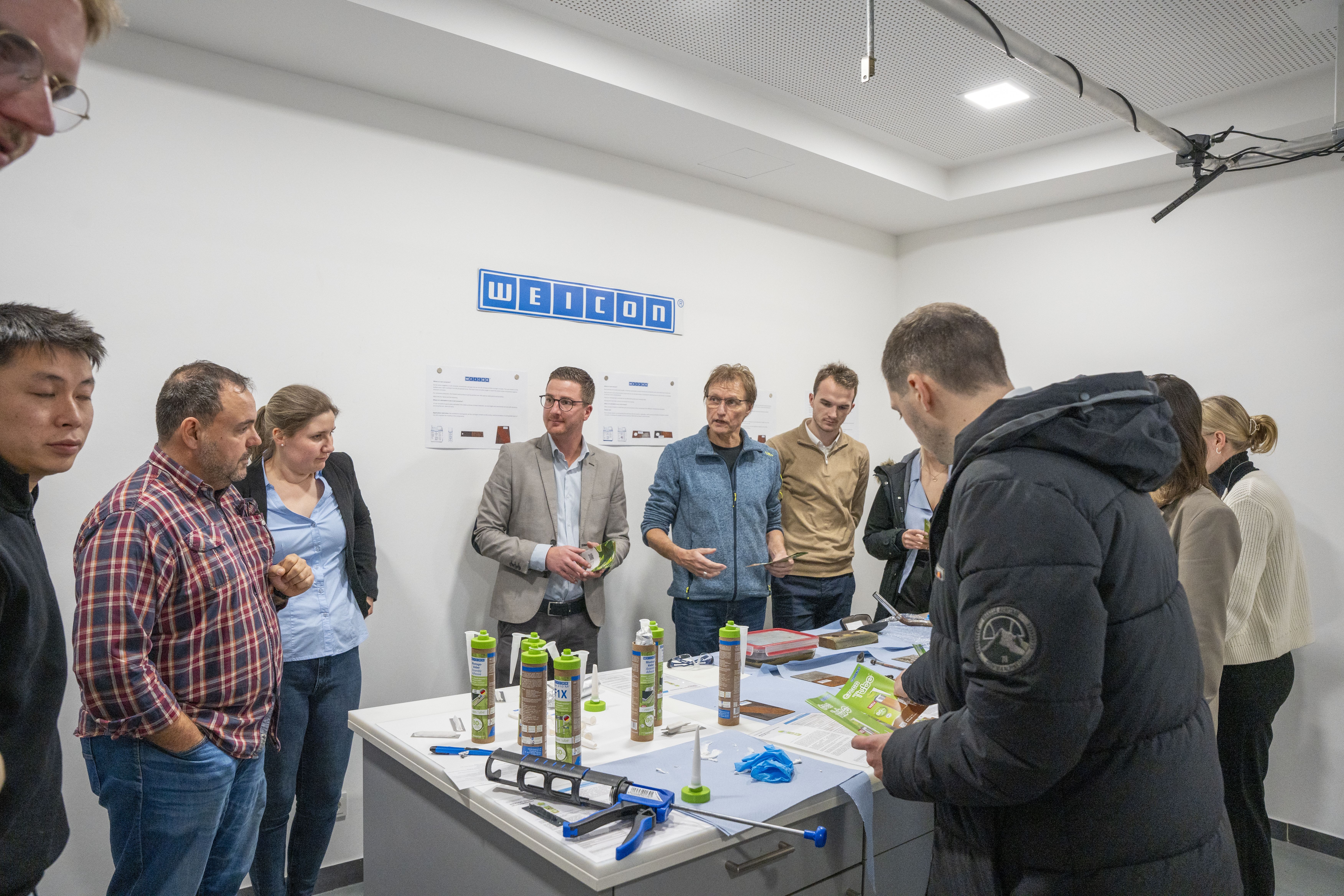 Mehrere Menschen sind in einem Schulungslabor und stehen um einen Tisch mit Produkten herum
