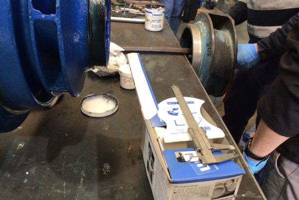 Technicians work on large industrial pump components surrounded by WEICON packaging, tools, and coating materials on a workbench.