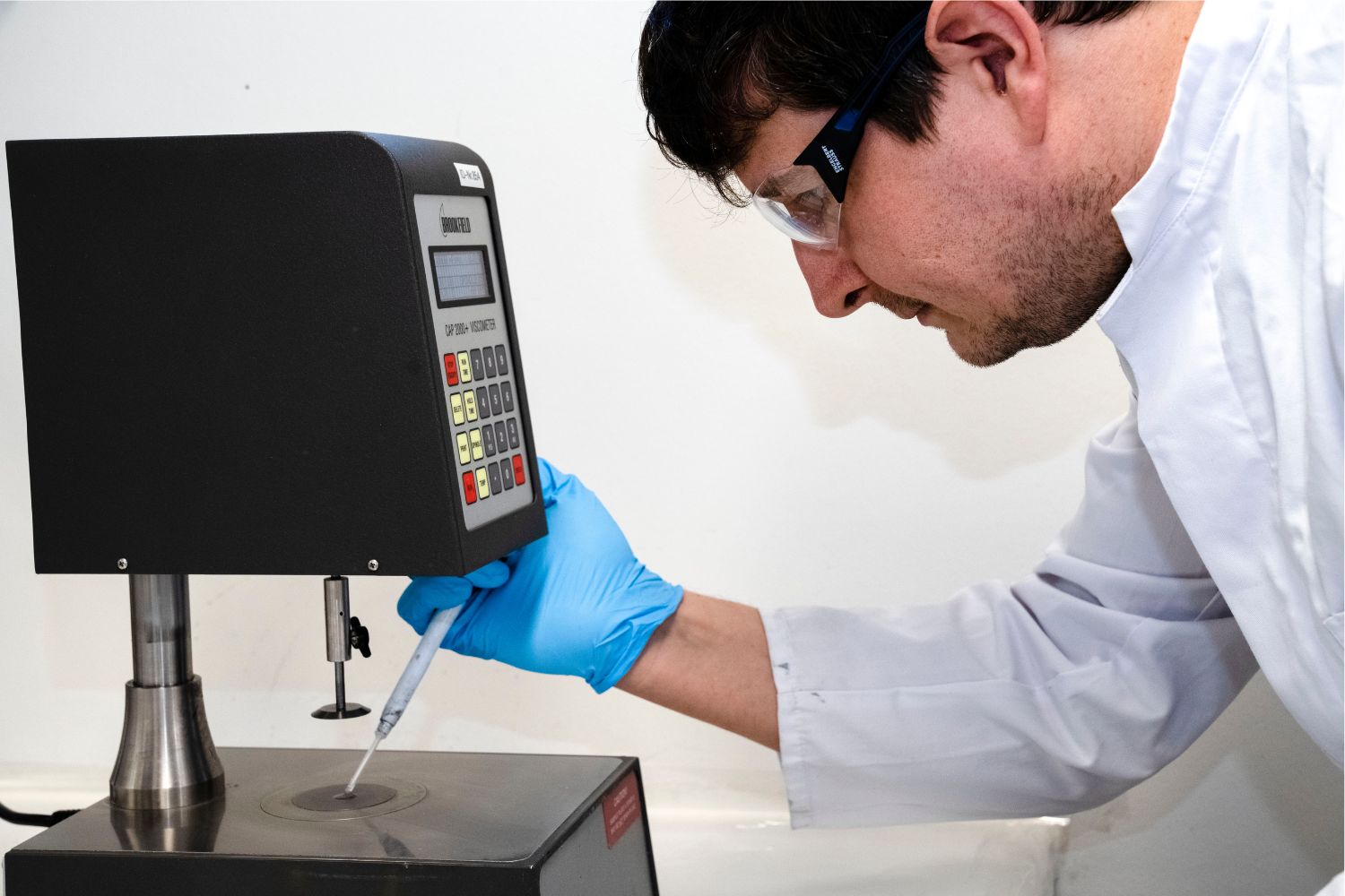 Mężczyzna w białym fartuchu nakłada coś z pipety na powierzchnię